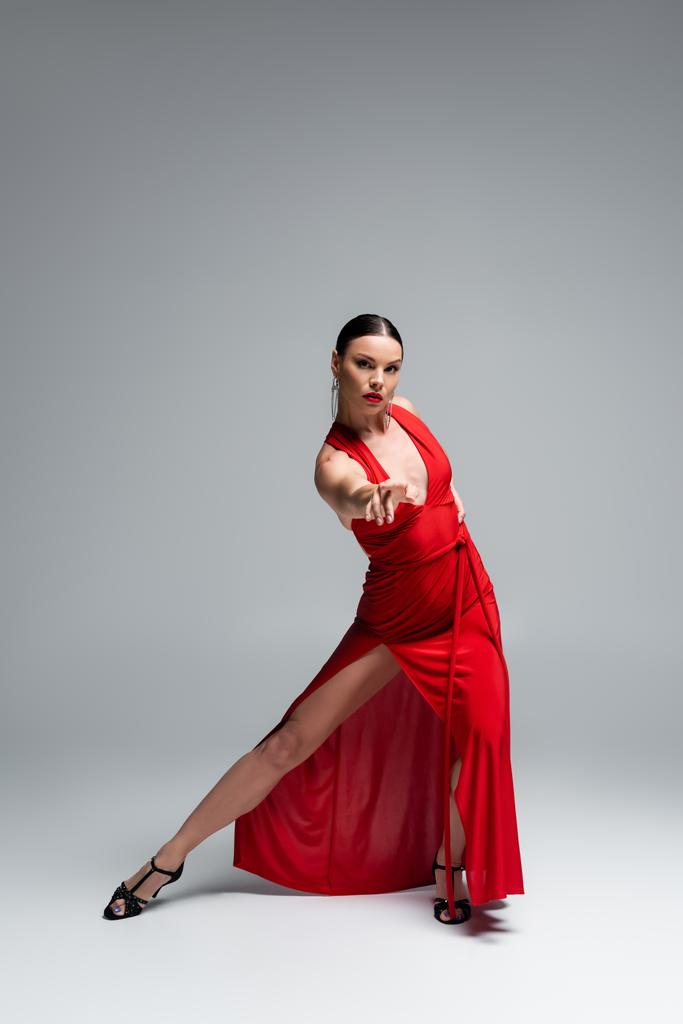Plná délka tanečnice v červených šatech při pohledu na kameru na šedém pozadí - Fotografie, Obrázek