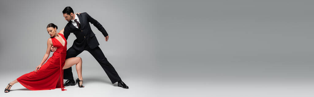 Stylish man in suit performing tango with woman on grey background, banner  - Photo, Image