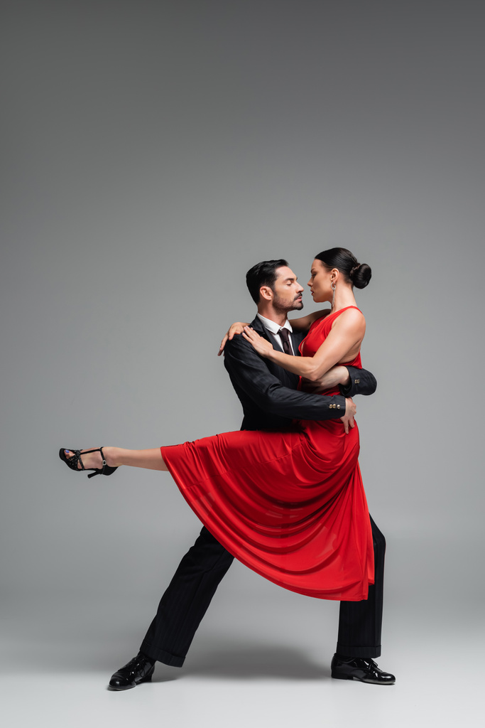 Vista lateral de la pareja bailarina en vestido rojo sobre fondo gris - Foto, Imagen