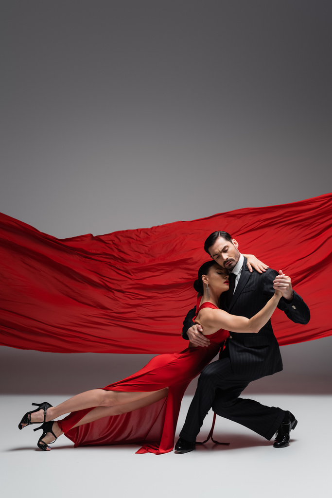 Elegante paar handen vasthouden tijdens het uitvoeren van tango op grijze achtergrond met rode stof  - Foto, afbeelding