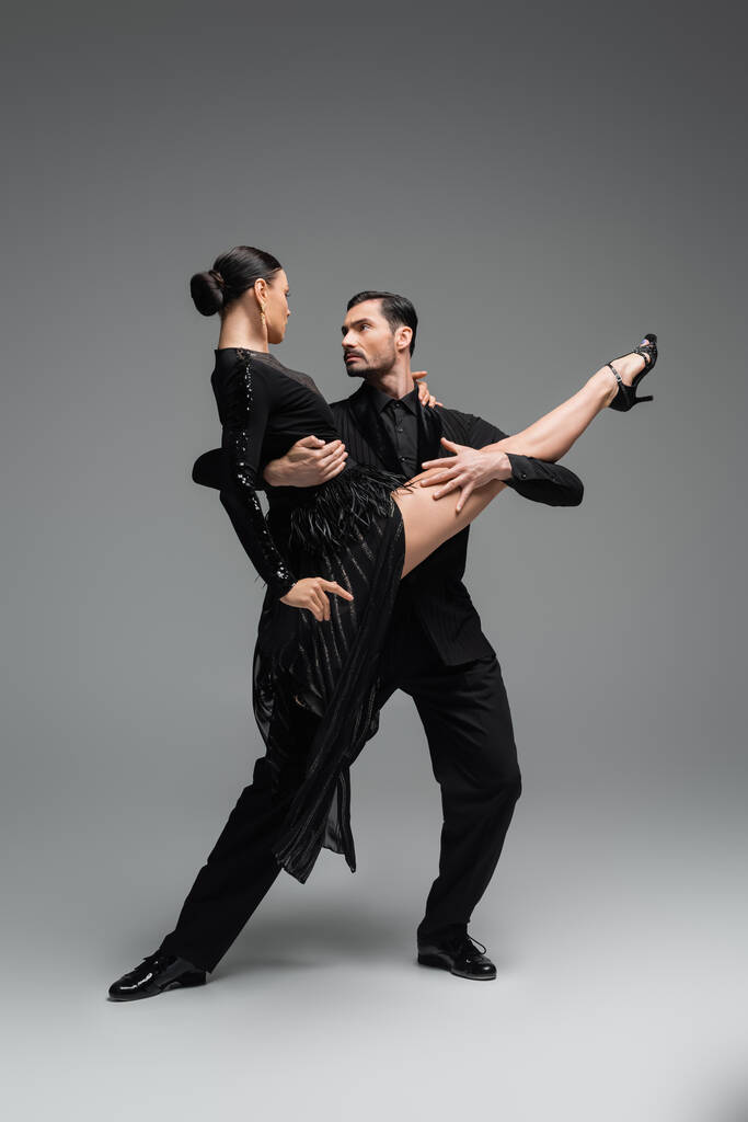 Profesyonel dansçılar, gri arka planda tango yaparken birbirlerine bakarlar. - Fotoğraf, Görsel