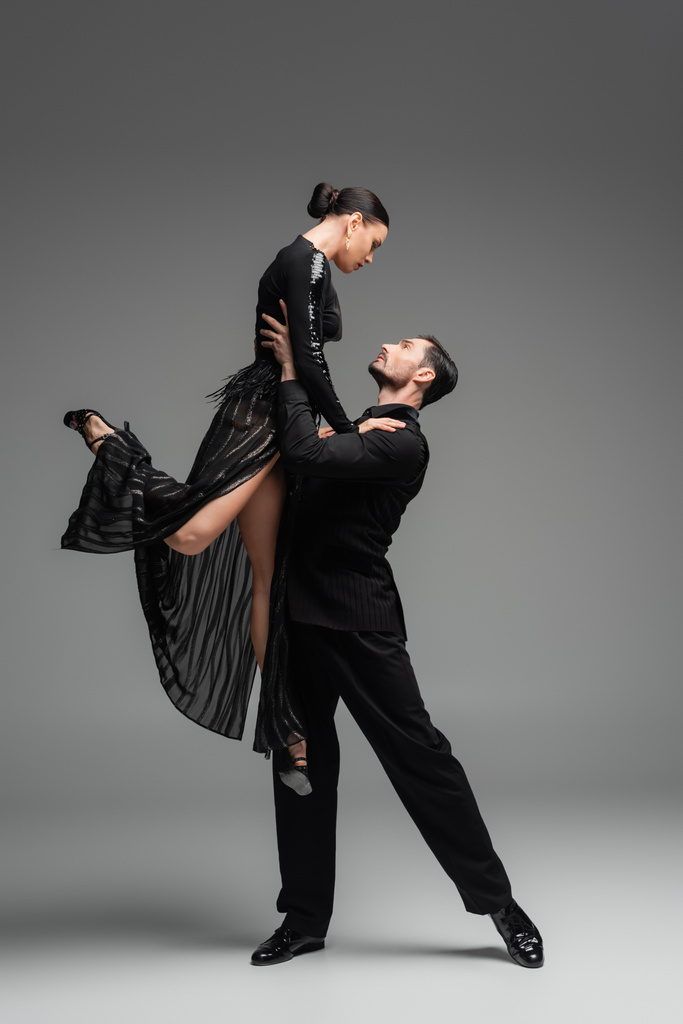 Zijaanzicht van professionele ballroom danseres hijs partner op grijze achtergrond - Foto, afbeelding