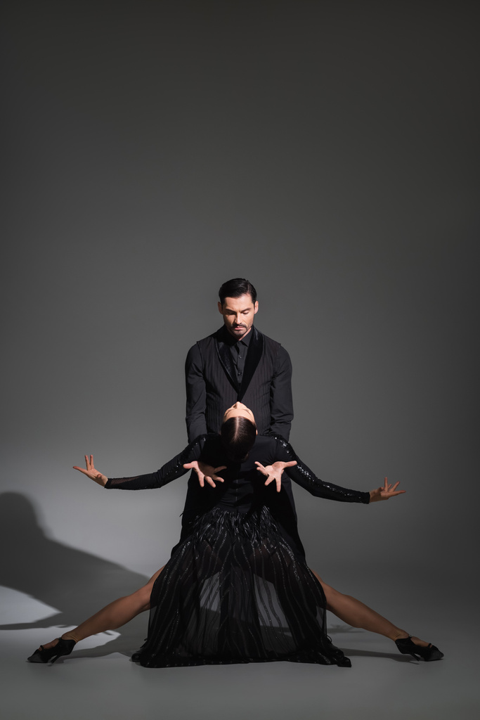 Dancer in suit performing tango with woman in black dress on grey background with shadow  - Photo, Image