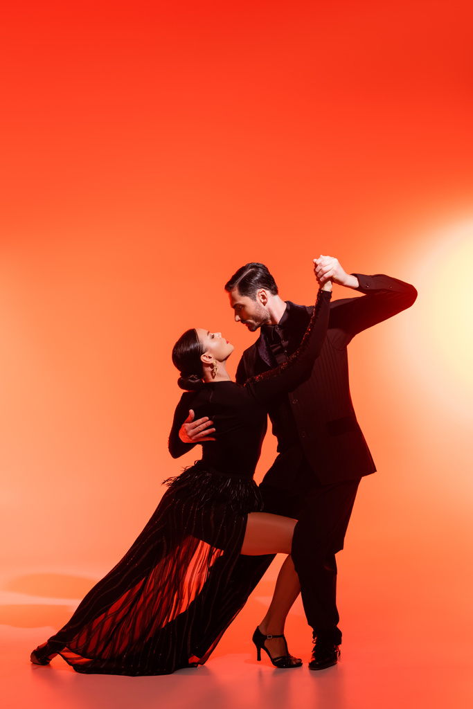 Вид збоку професійних танцюристів, які виконують танго на червоному тлі
  - Фото, зображення