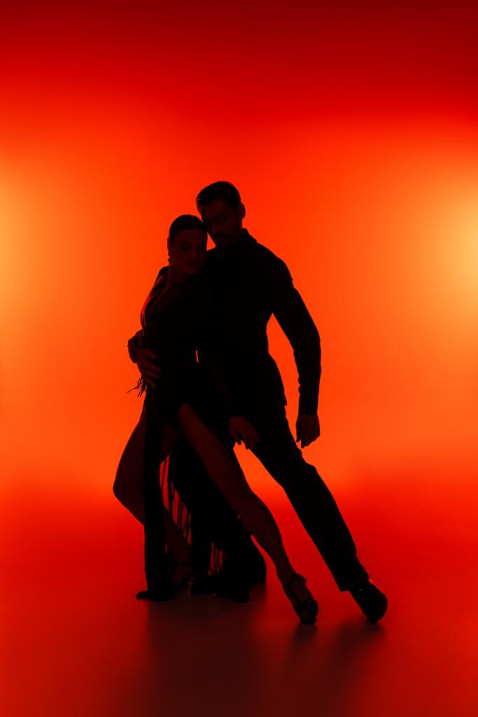 Silueta de bailarines de salón realizando tango sobre fondo rojo  - Foto, Imagen
