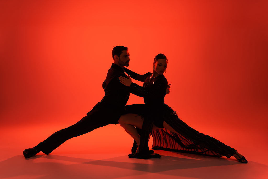 Silhouet van elegant koppel dansende tango op rode achtergrond  - Foto, afbeelding
