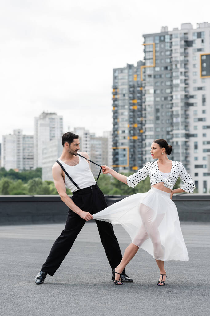 Vista lateral de bailarina con estilo en tacones bailando con pareja en el techo  - Foto, imagen