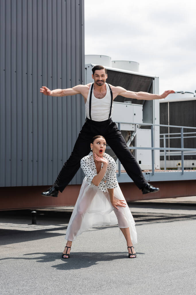 Усміхнений танцюрист стрибає біля шокованого партнера на даху будівлі на відкритому повітрі
  - Фото, зображення