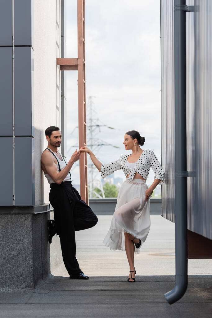 Smiling professional dancer touching hand of partner on rooftop of building outdoors  - Photo, Image