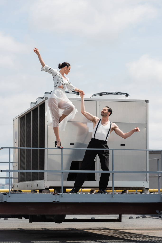 ヒールのにこにこダンサーと屋外の建物の屋根の上にパートナーの手を保持スカート  - 写真・画像
