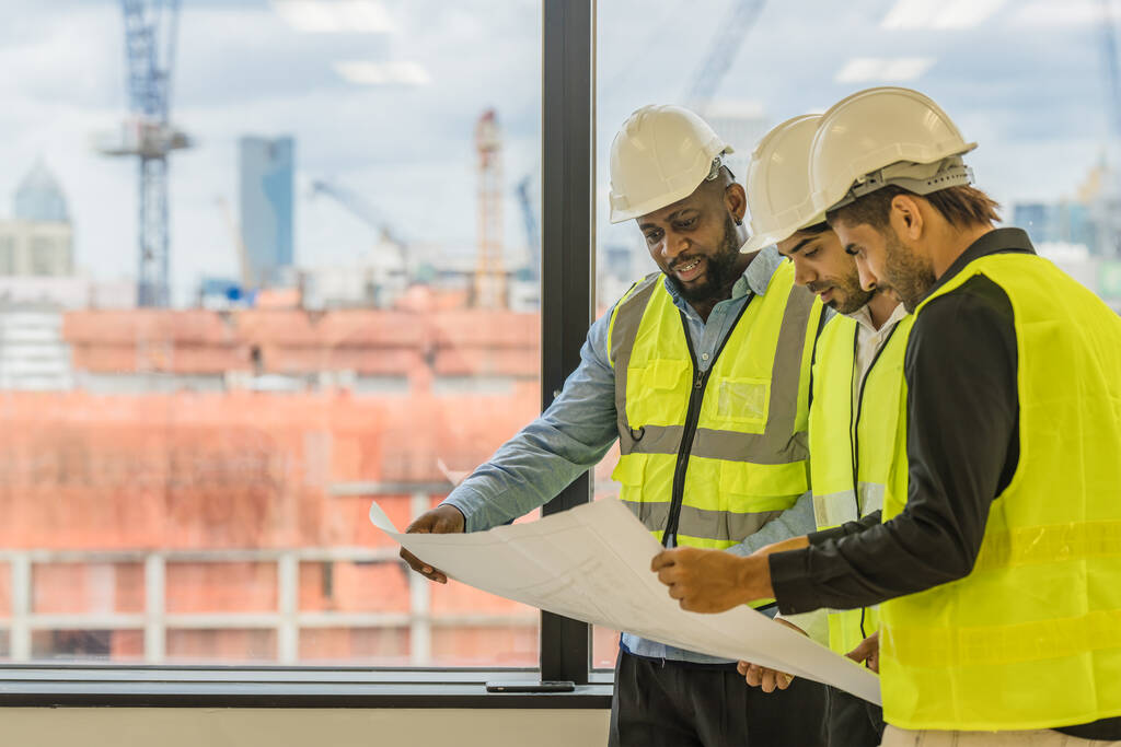 строительная отрасль и бизнес-фон трех инженеров-строителей, занимающихся проектированием и совместной работой на фоне строительной площадки - Фото, изображение