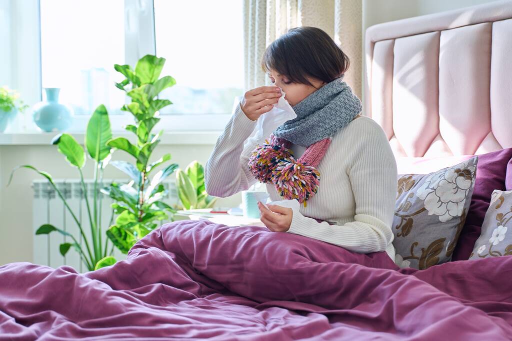 Chora kobieta trzymająca chusteczkę, kichająca, wycierająca nos, siedząca w domu w łóżku. Problemy zdrowotne, sezon zimnej grypy, styl życia, koncepcja ludzi - Zdjęcie, obraz