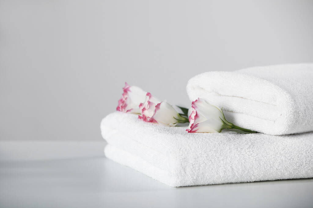Asciugamani morbidi piegati con fiori sul tavolo bianco, spazio per il testo - Foto, immagini