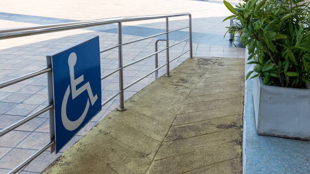 Señal de camino para discapacitados en frente del edificio. Símbolo de tráfico de señal para discapacitados en el suelo delante de la rampa para silla de ruedas de apoyo. Señal de camino para discapacitados frente a la cafetería en el paisaje verde de la naturaleza. - Foto, imagen