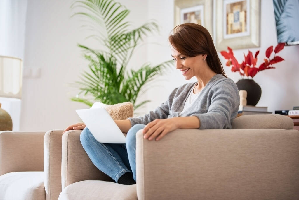 Snímek atraktivní ženy středního věku sedící na gauči při používání notebooku. Krásná žena v neformálním oblečení.  - Fotografie, Obrázek