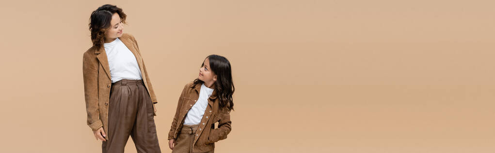femme gaie et fille en vêtements d'automne à la mode se regardant isolés sur beige, bannière - Photo, image