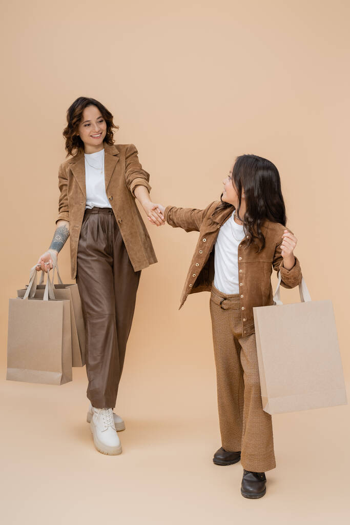 trendi lány bevásárló táskák fogja kezét vidám és elegáns anya bézs háttér - Fotó, kép