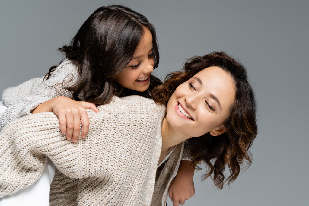 usmívající se žena v podzimním oblečení při pohledu na šťastnou dceru, zatímco piggybacking ji izolované na šedé - Fotografie, Obrázek