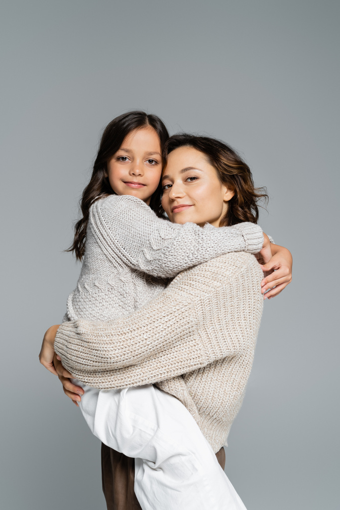 happy woman and smiling girl in stylish knitwear hugging and looking at camera isolated on grey - Photo, Image
