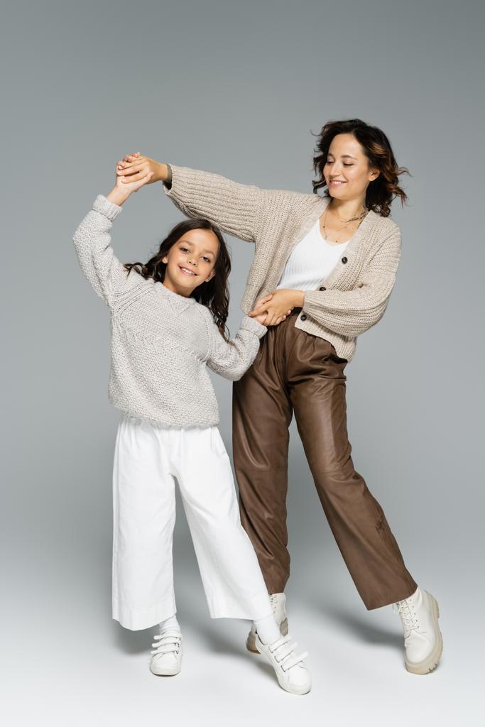 excited mother and child in autumn clothes holding hands and dancing on grey background - Photo, Image