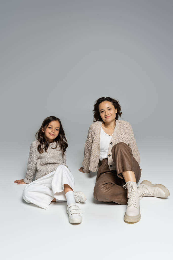 barna anya és lánya kötött ruha és nadrág ül szürke háttér - Fotó, kép