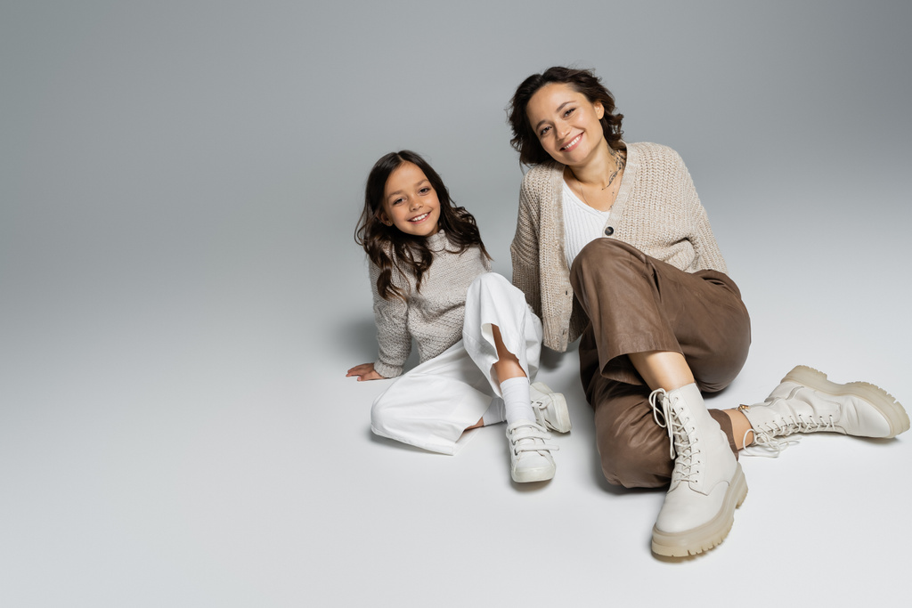lány és anya divatos és meleg ruhák ül és mosolyog a kamera szürke háttér - Fotó, kép