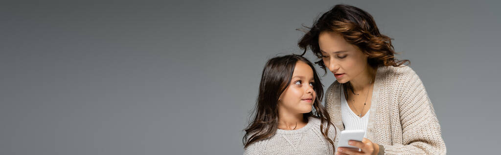 mère et fille en tricot chaud se regardant près d'un smartphone isolé sur gris, bannière - Photo, image