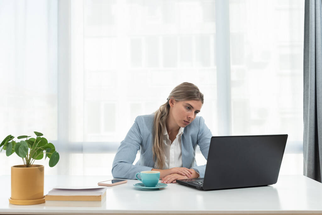 Nuori turhautunut liiketoiminnan nainen toimistotyöntekijä yrittää keskittyä työhönsä, kun hän istuu yrityksen toimistossa vanha kannettava tietokone ja hidas internet-yhteys. - Valokuva, kuva