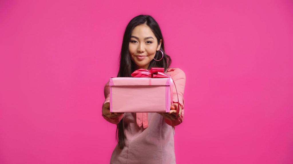potěšen mladý asijské žena držení zabalený dárek izolovaný na růžový  - Fotografie, Obrázek