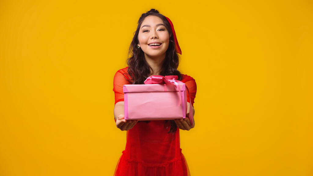 pozytywny i młody Azji kobieta dając opakowany prezent na żółty  - Zdjęcie, obraz