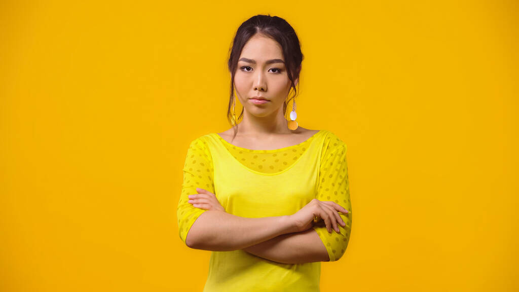insoddisfatta asiatica donna in piedi con le braccia incrociate isolato su giallo  - Foto, immagini