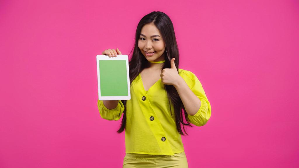 onnellinen aasialainen nainen tilalla digitaalinen tabletti vihreällä näytöllä ja näyttää kuin eristetty vaaleanpunainen   - Valokuva, kuva