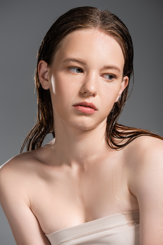 Mulher muito jovem com a pele molhada e ombros nus olhando para longe isolado em cinza  - Foto, Imagem