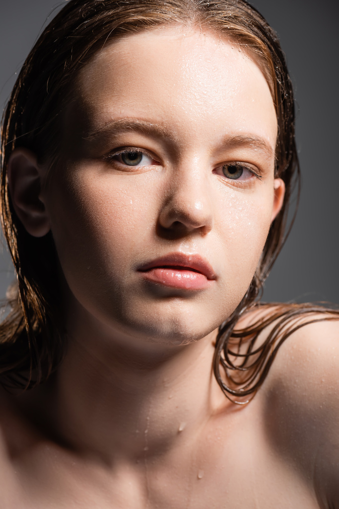 Modelo joven con cabello mojado y gotas de agua en el cuello mirando a la cámara aislada en gris  - Foto, Imagen