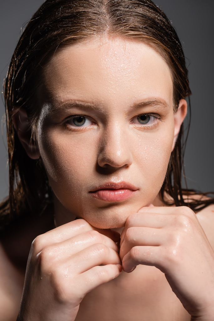 Πορτρέτο της όμορφης νεαρής γυναίκας με βρεγμένο δέρμα αγγίζοντας πηγούνι απομονωμένο σε γκρι  - Φωτογραφία, εικόνα