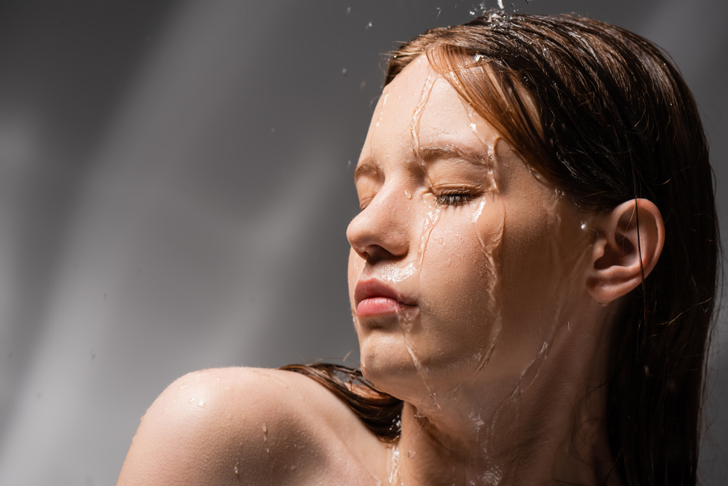 Красивая молодая женщина с голым плечом, стоящая под водой на абстрактном сером фоне  - Фото, изображение