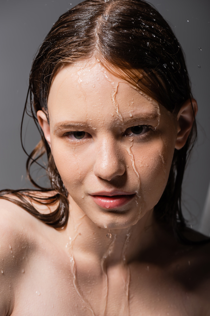 Портрет молодої жінки з водою на обличчі і волоссям, дивлячись на камеру на сірому фоні
  - Фото, зображення