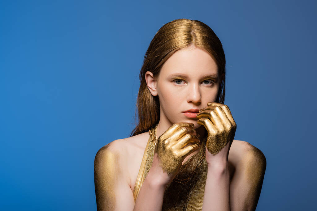 Ritratto di donna dai capelli biondi con vernice dorata su mani isolate su blu  - Foto, immagini