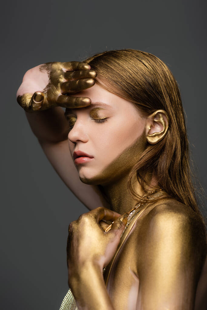 Vrouw met gouden glitter op de huid poseren met gesloten ogen geïsoleerd op grijs  - Foto, afbeelding