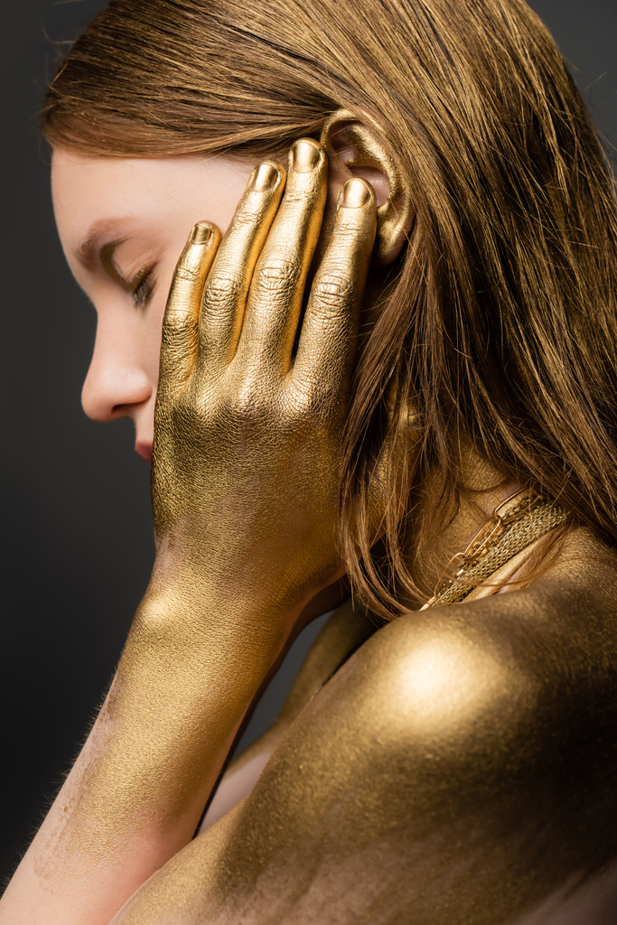 Oldalnézet fiatal nő arany festék érintő fül elszigetelt szürke  - Fotó, kép
