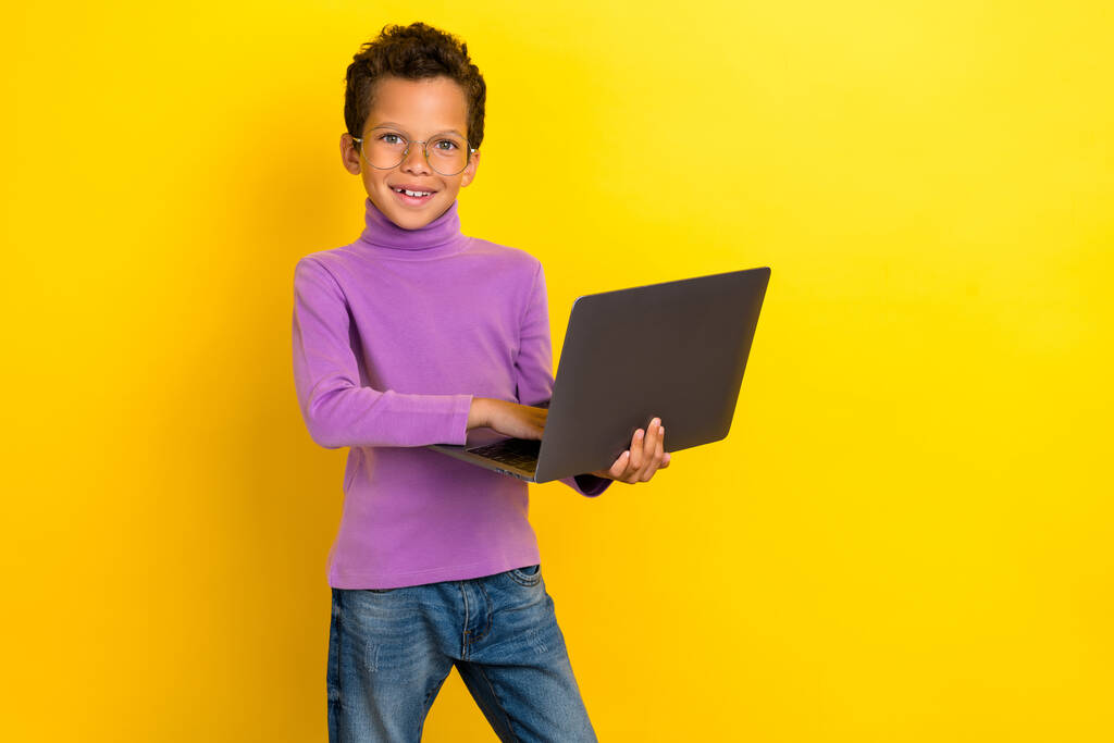 Porträt von fröhlichen intelligenten Schulkind hols verwenden drahtlose Netbook isoliert auf gelbem Hintergrund. - Foto, Bild