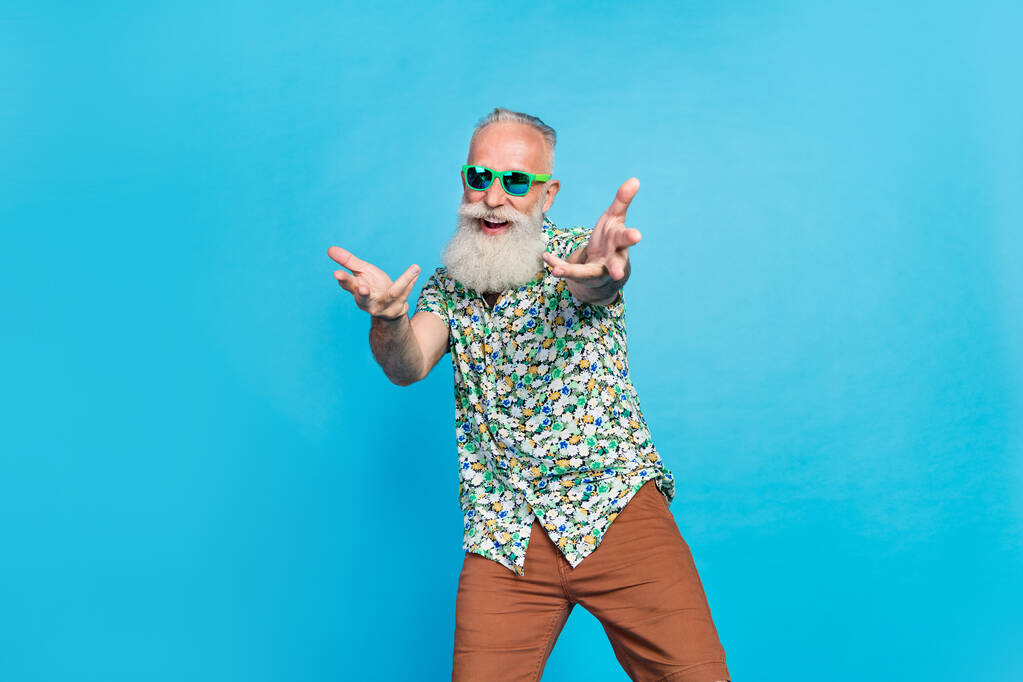 Foto de pensionista de edad avanzada usar traje elegante gafas de sol verde recoger fresco abuelo macho invitando a evento aislado sobre fondo de color azul. - Foto, imagen