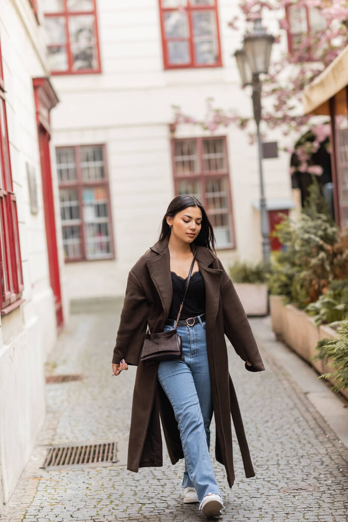 молодая и красивая женщина в модной осенней одежде ходит по узкой улице в Праге - Фото, изображение