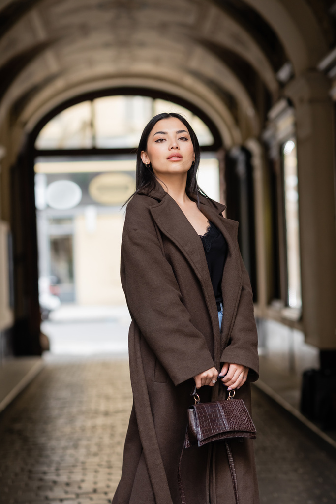 молодая женщина в модном осеннем пальто держа сумочку и глядя на улицу в Праге - Фото, изображение