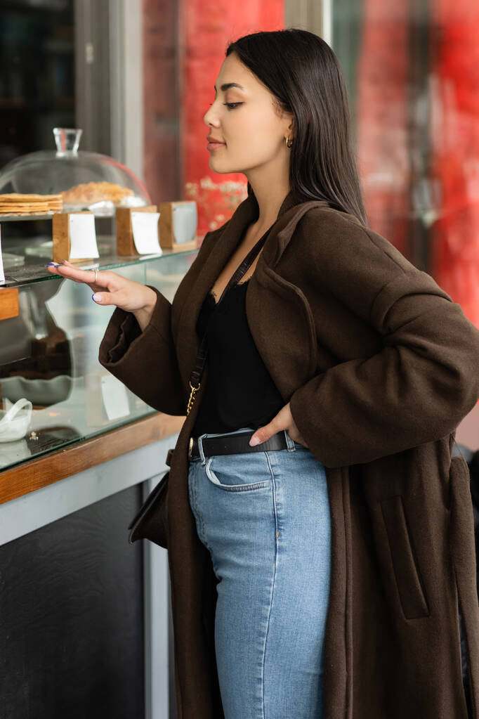 boční pohled na módní brunetky žena dotýkající se vitríny cukrárny v Praze - Fotografie, Obrázek