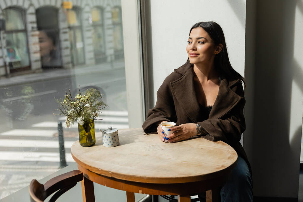 glückliche Frau blickt auf die Straße, während sie in einem Prager Café am Fenster sitzt - Foto, Bild