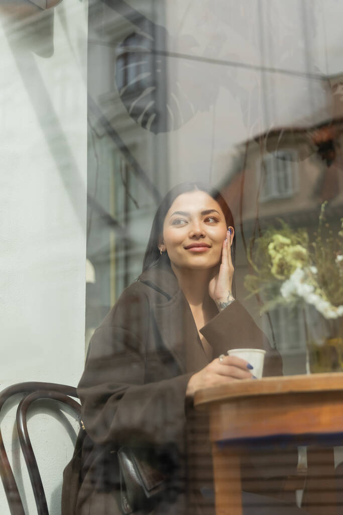 szczęśliwa kobieta patrząc na zewnątrz siedząc w pobliżu okna w kawiarni Praga - Zdjęcie, obraz