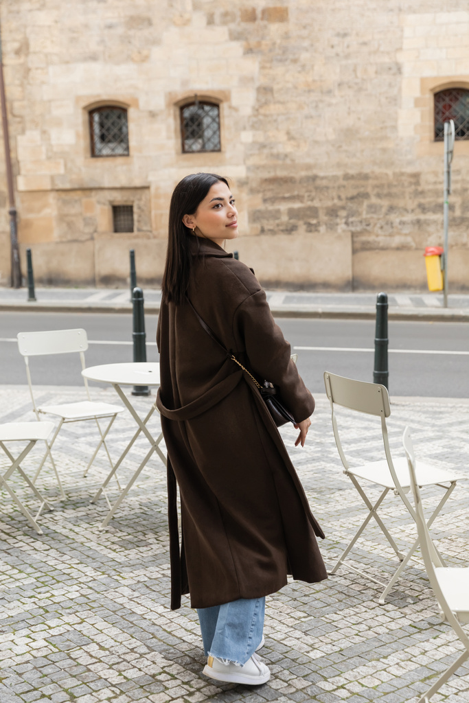 Mujer con estilo en abrigo caminando cerca de la silla de café al aire libre en Praga  - Foto, imagen