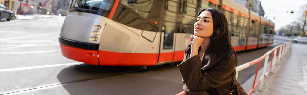 Módní mladá žena v kabátě stojící u silnice s tramvají na ulici v Praze, prapor  - Fotografie, Obrázek