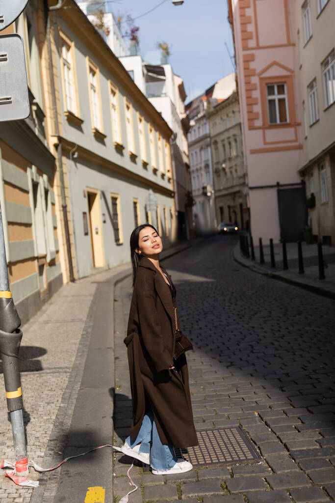 Bruneta žena v kabátě kráčí po rozmazané městské ulici v Praze  - Fotografie, Obrázek